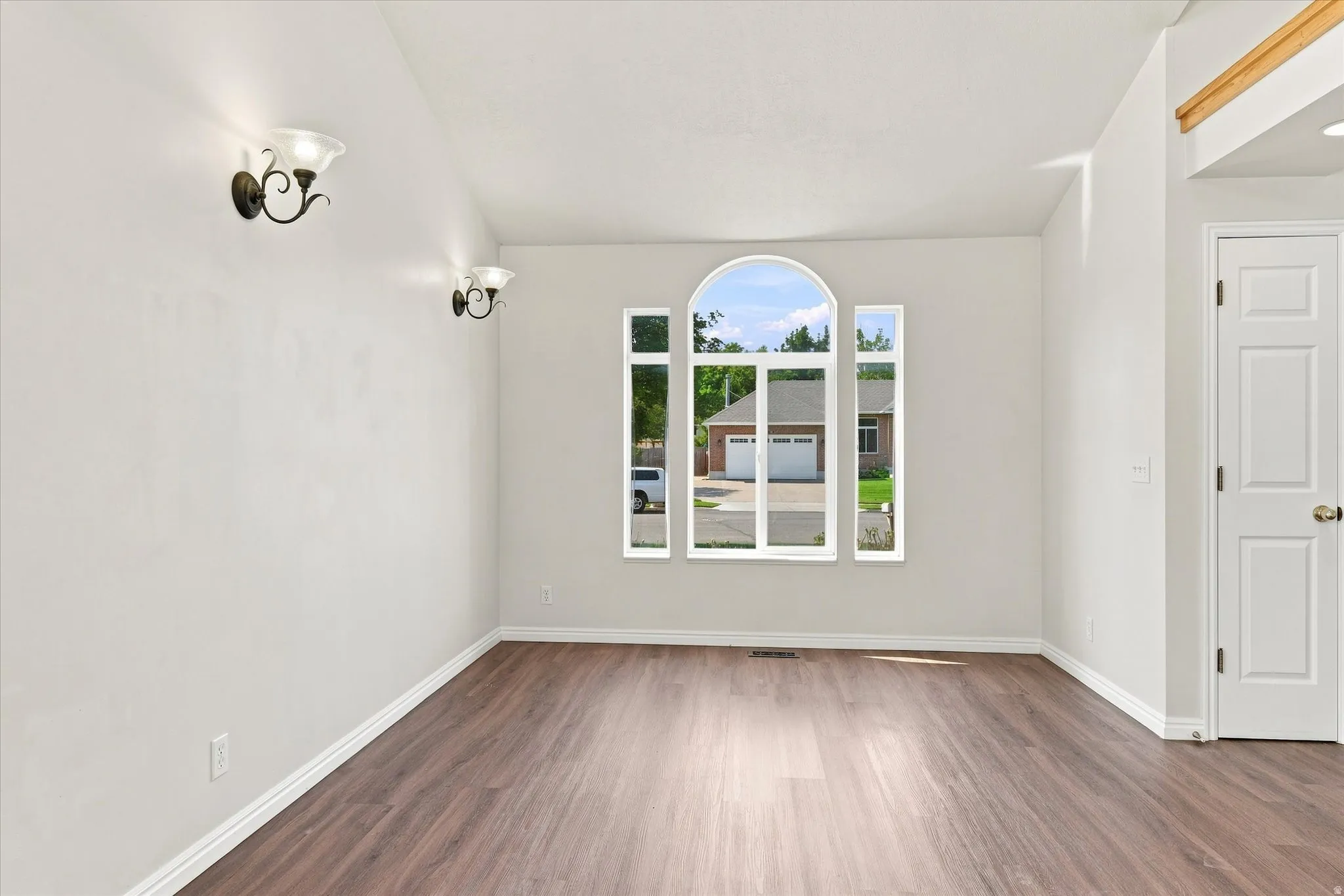 Wood-finish flooring, arched window, wall sconce lighting, vaulted ceiling, and paneled door