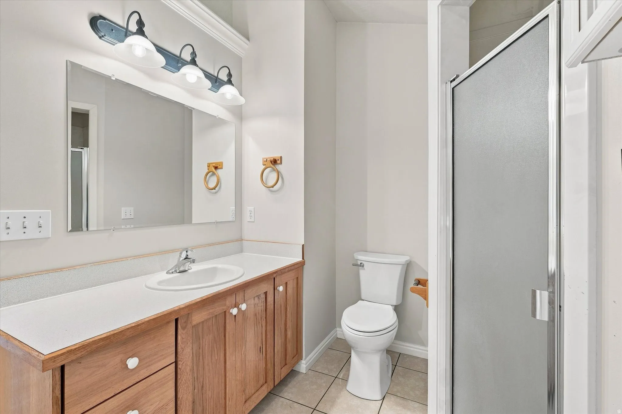 Bathroom featuring a wood-finish vanity with a white countertop, an integrated sink, a three-light vanity fixture, and a glass-enclosed shower