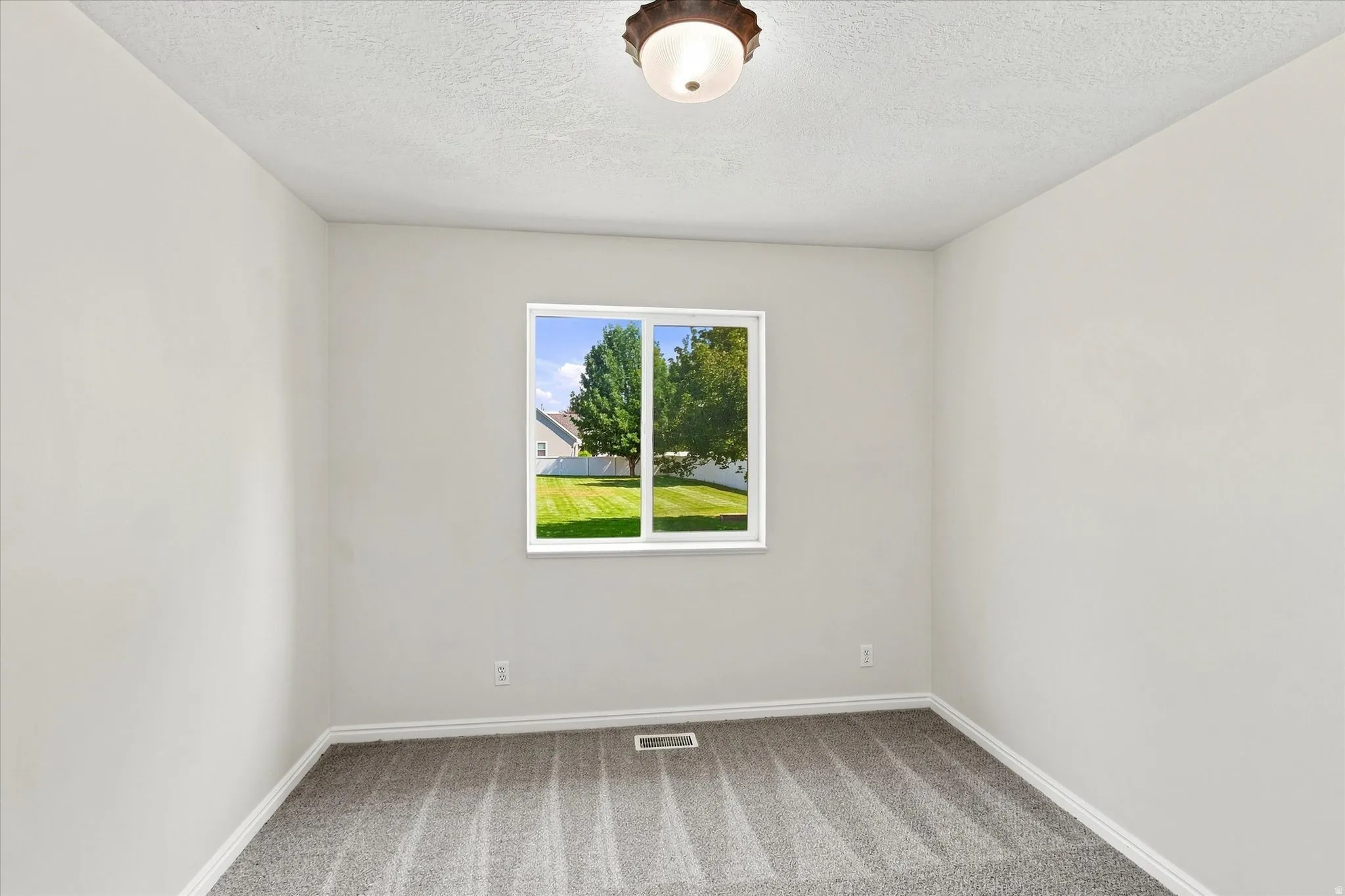 Bright room featuring a large window, neutral wall paint, and textured carpeting
