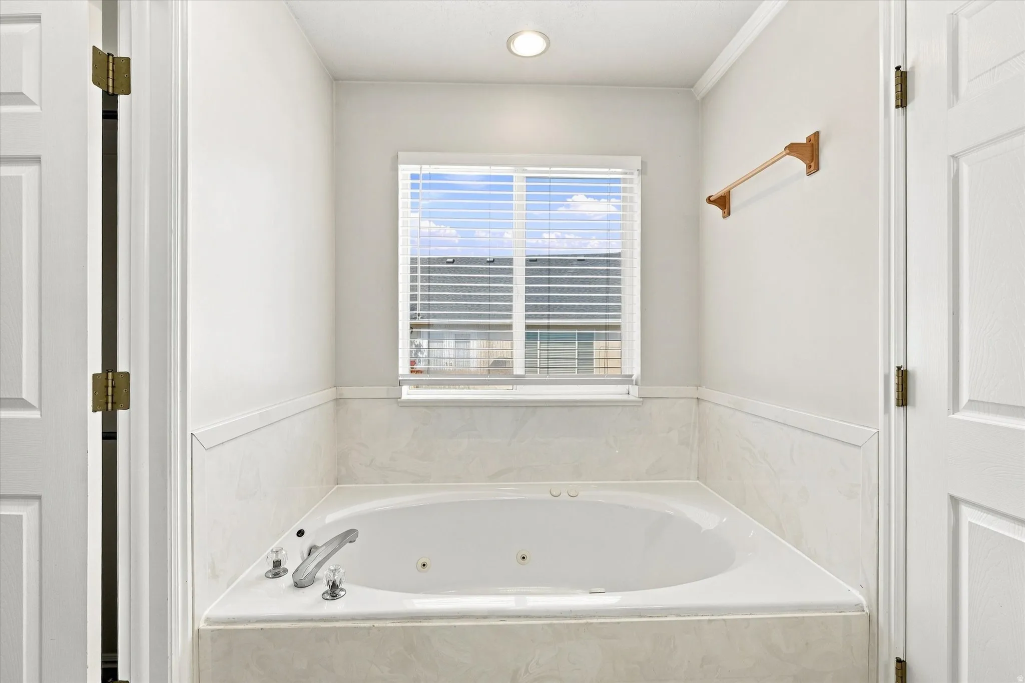 Built-in soaking tub with a tiled surround, recessed lighting, and a window with blinds