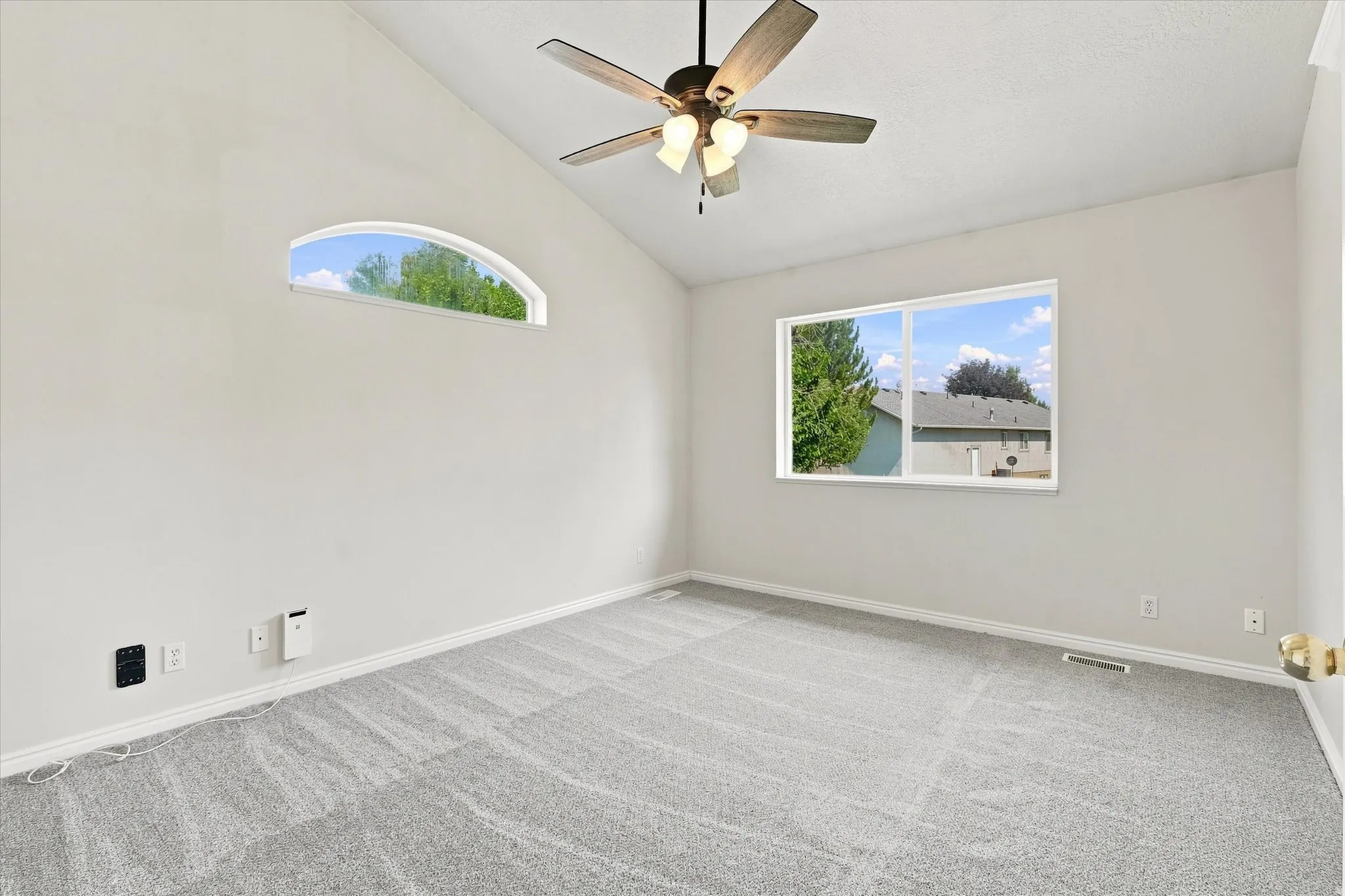Vaulted ceiling with a ceiling fan, arched window, standard window, and light gray carpet flooring