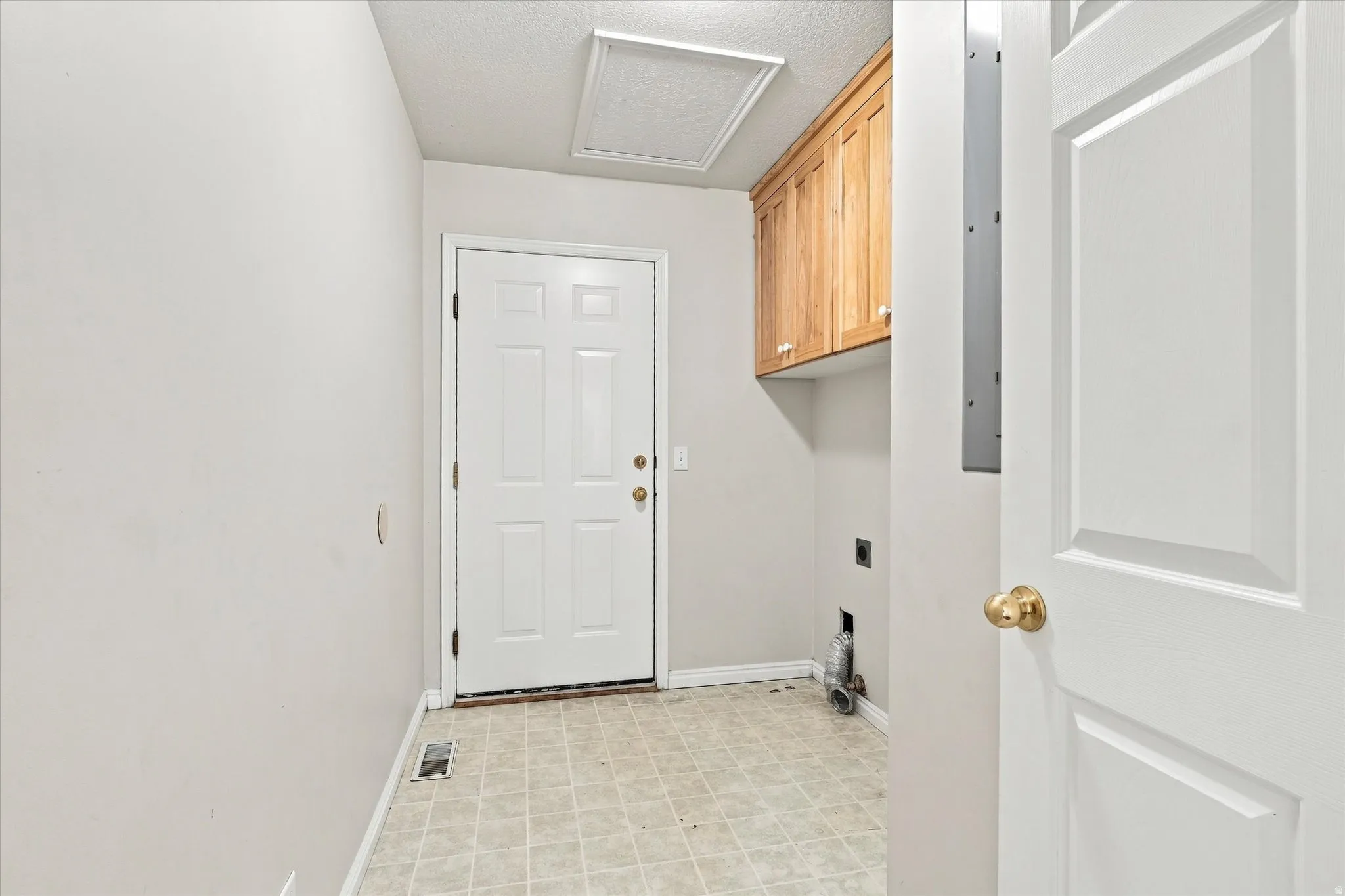 Utility room featuring light wood-finish cabinetry, patterned floor tiles, and a white paneled door