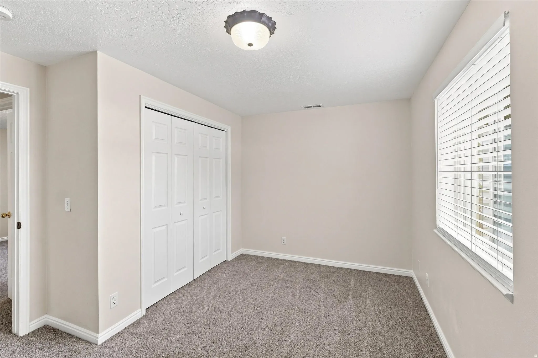 Light-colored walls, patterned carpeting, white window blinds, and white bi-fold closet doors