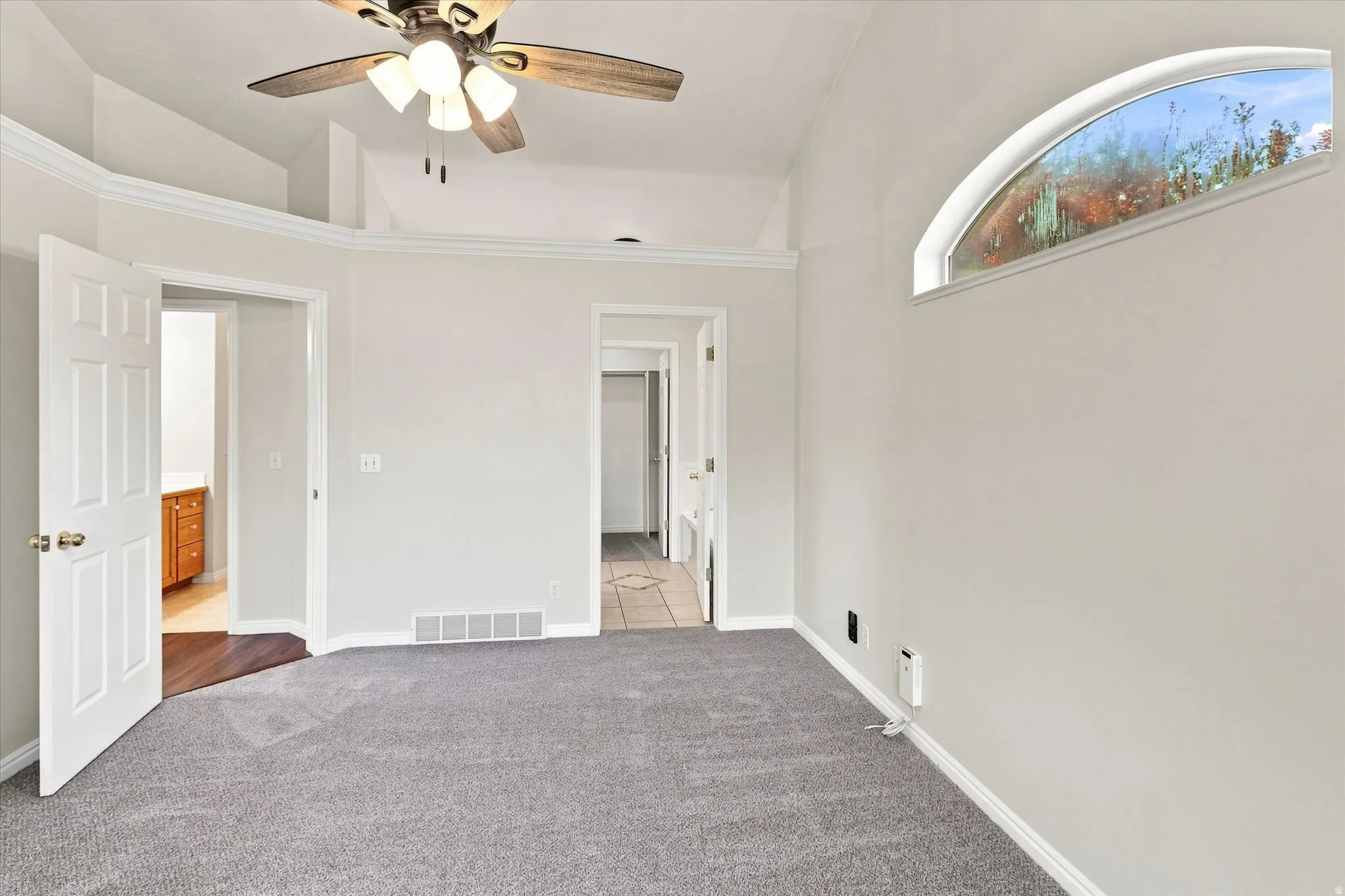 Recessed arched window, vaulted ceiling, ceiling fan, grey carpet, and white trim