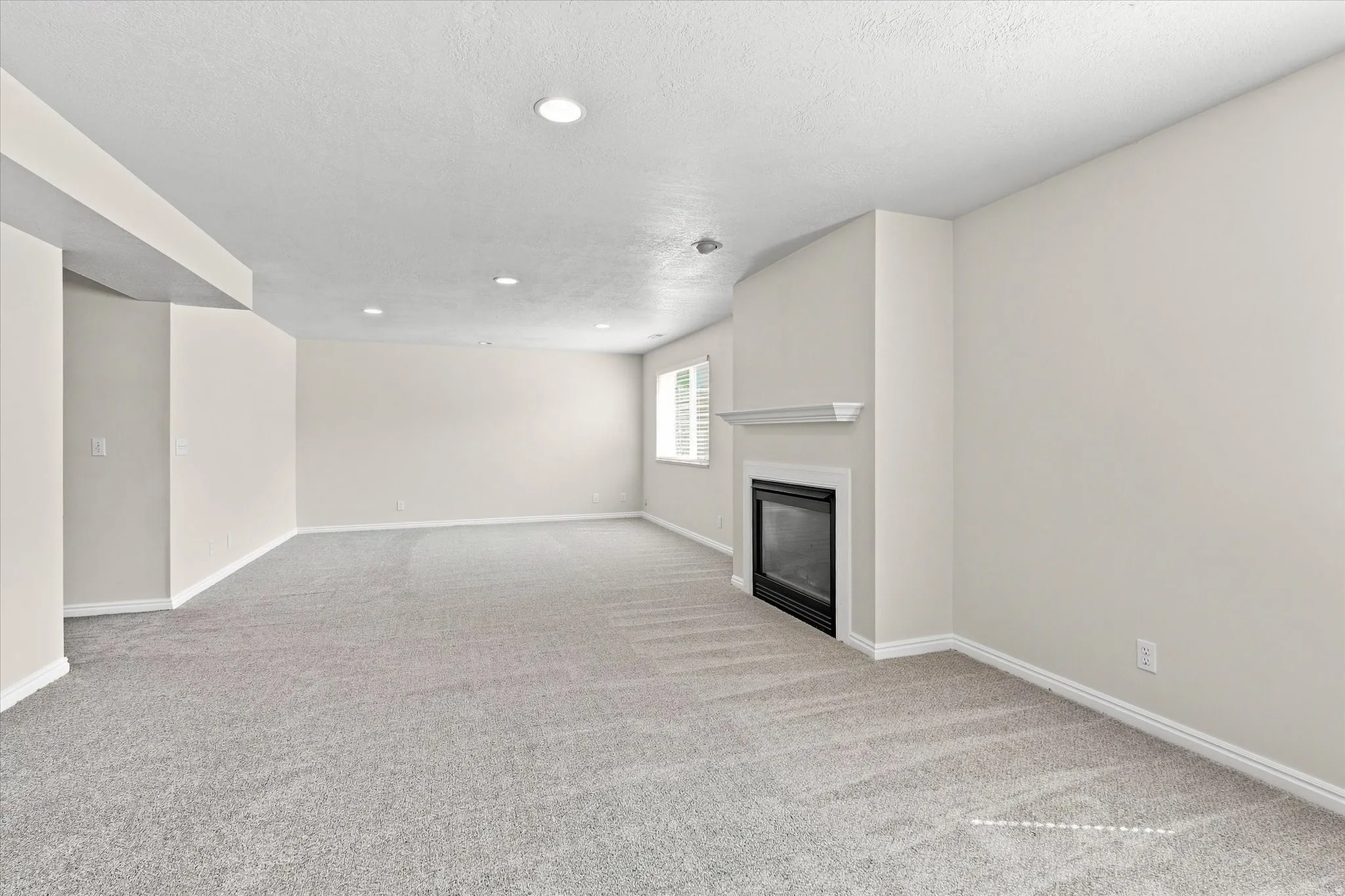 Recessed ceiling lighting, light gray carpeting, neutral wall finishes, fireplace with white mantel, and window with white shutters