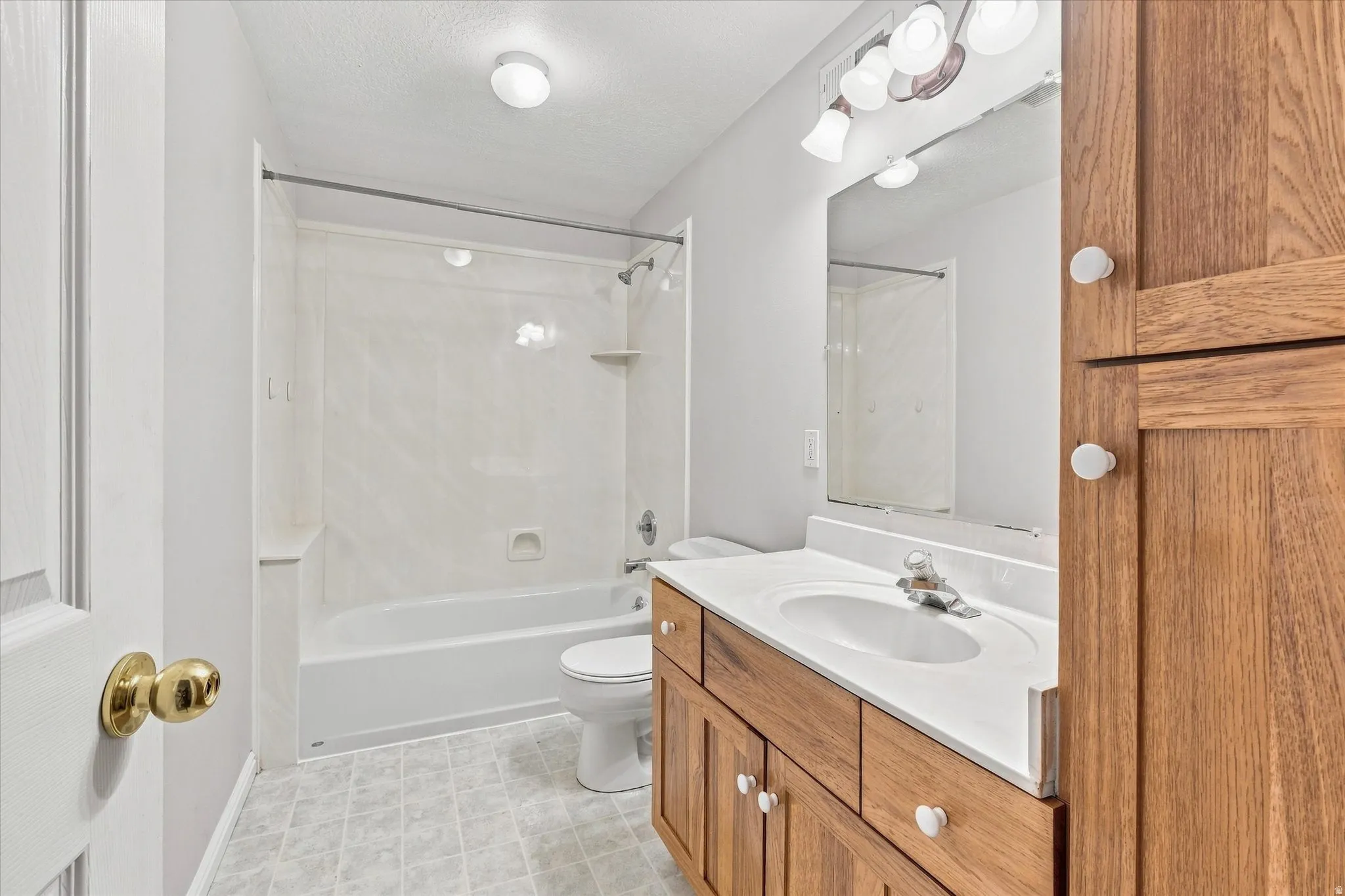Bathroom featuring a wood-finish vanity with a single basin sink, integrated mirror, and a shower-tub combination
