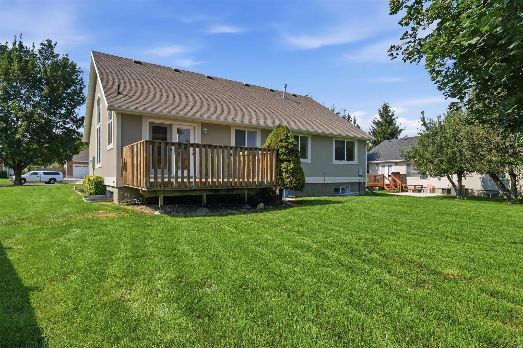 Expansive green lawn with a wood-plank deck, stucco exterior, and multi-pane windows