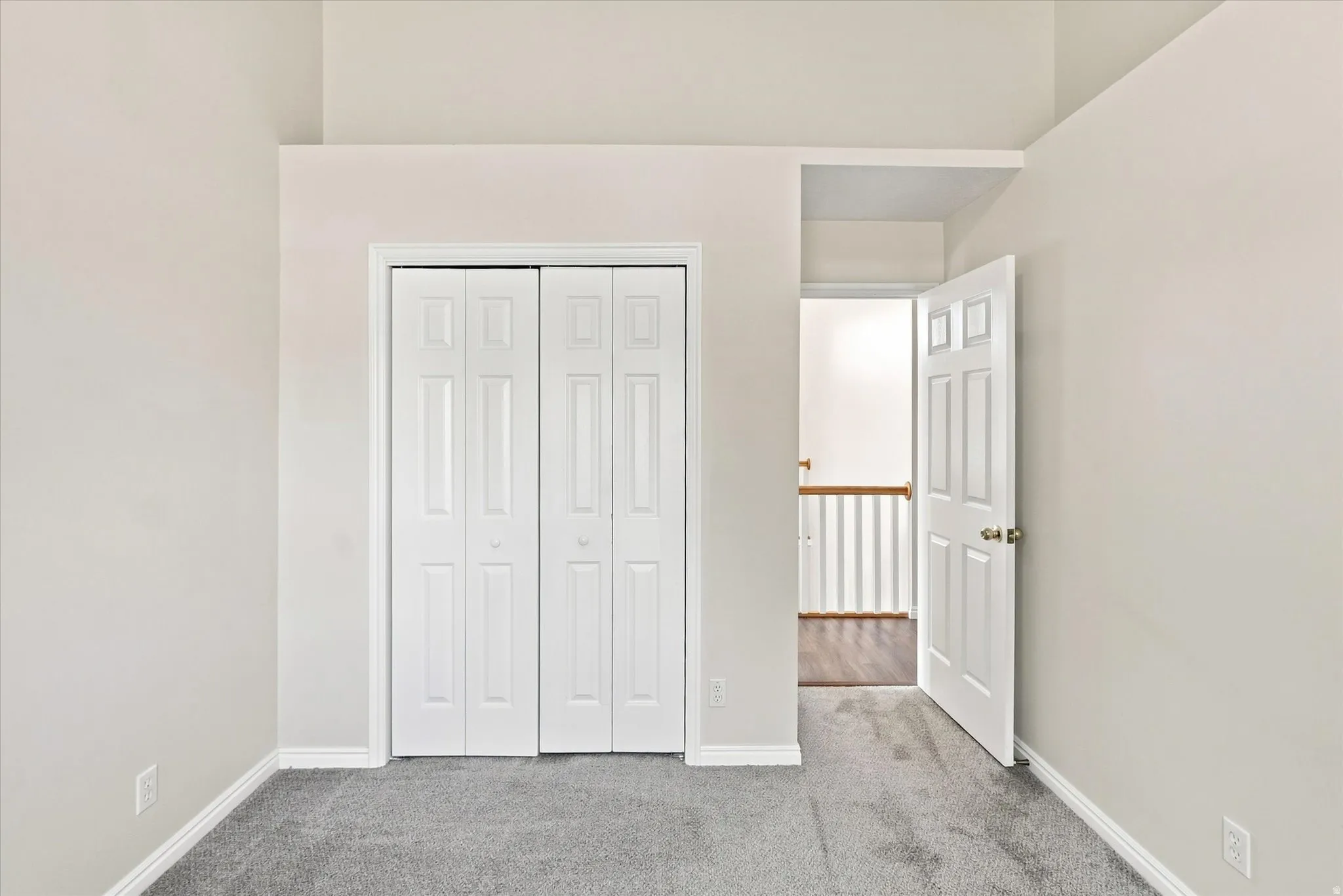 Vaulted ceiling with light-toned walls, grey carpeting, and white bi-fold closet doors
