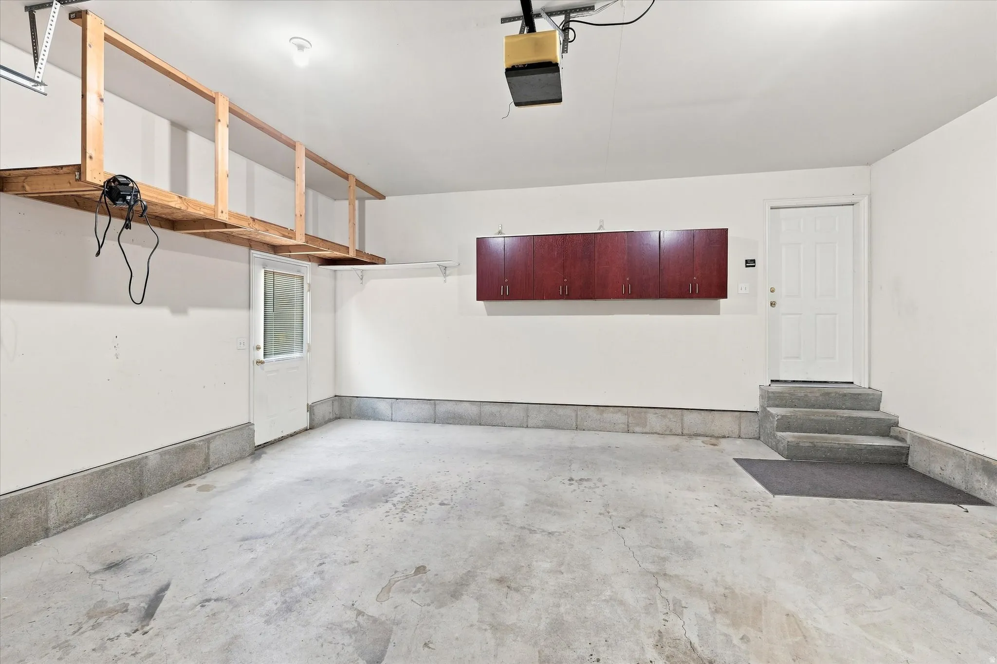 Attached garage featuring concrete flooring, built-in overhead storage, and wall-mounted cabinetry