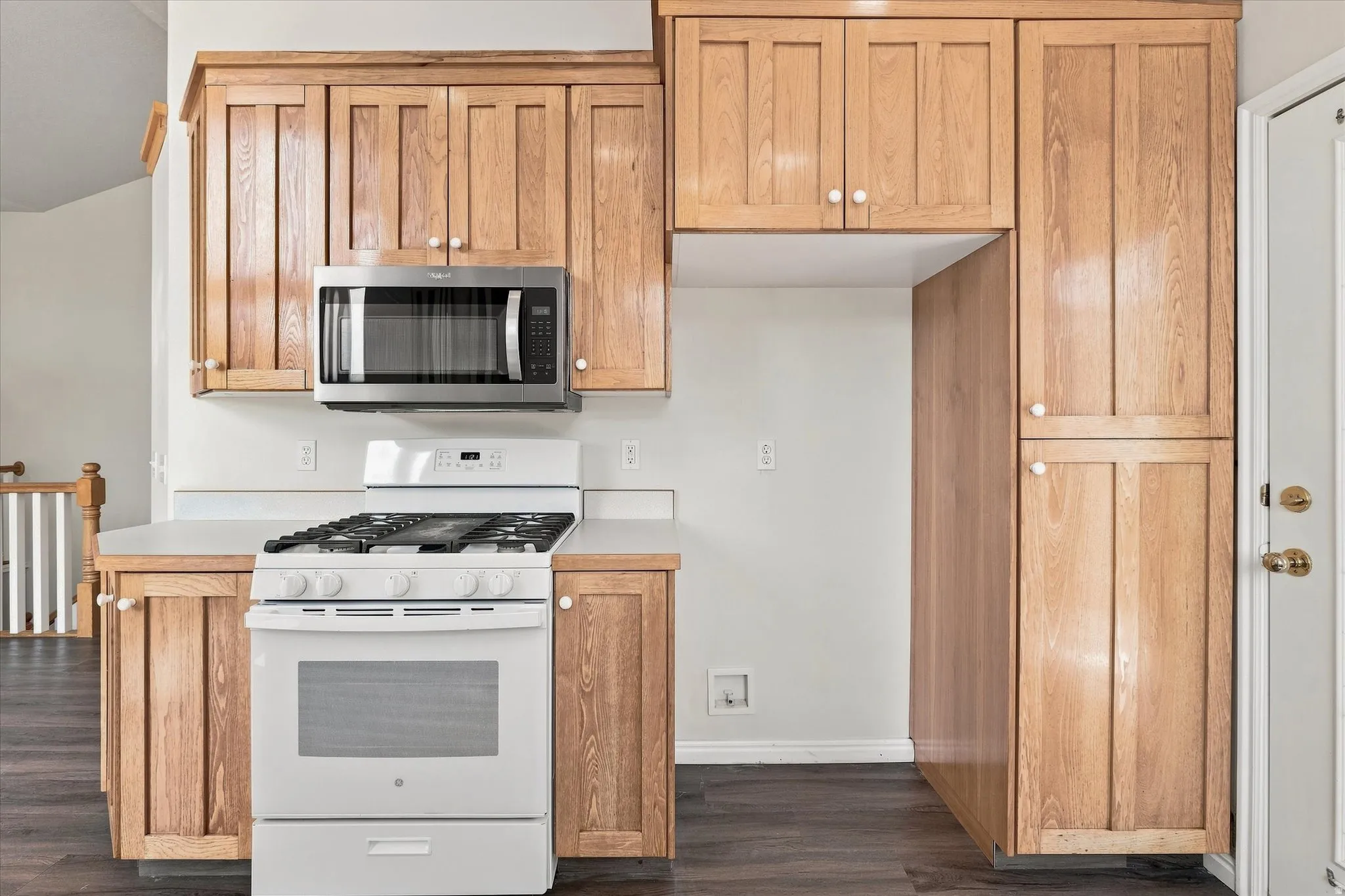 Wood-finish cabinetry with white knob hardware, stainless steel microwave, white gas range, and light-toned countertops