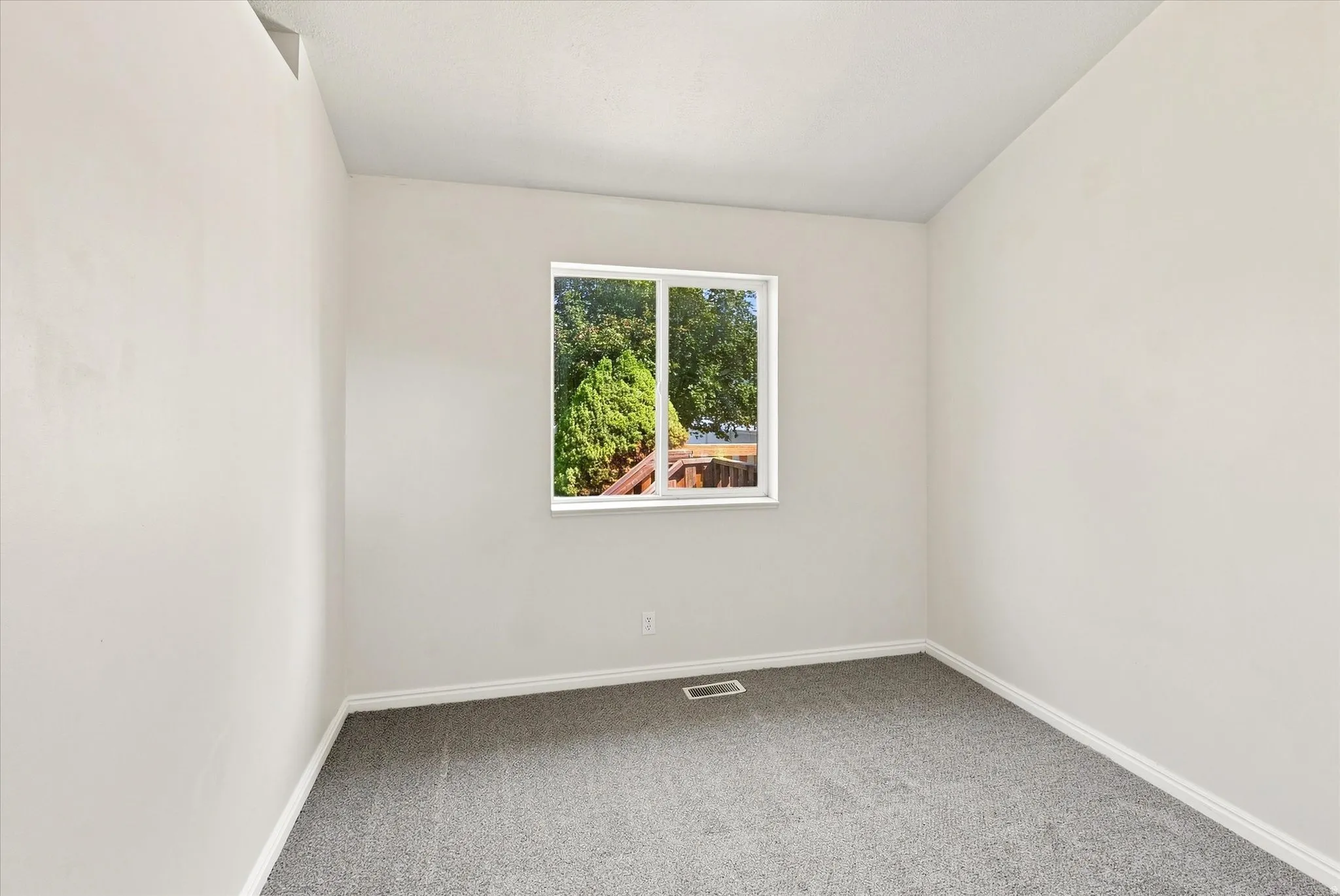 Grey carpet flooring, white painted walls, white trim, and a single window with white framing