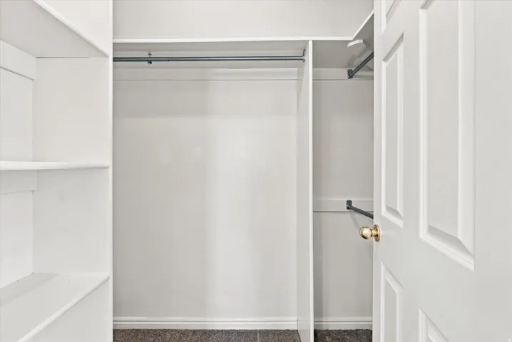 Built-in shelving, multiple hanging rods, paneled door, and brass-finish hardware