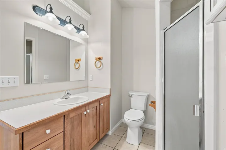 Bathroom featuring a wood-finish vanity with a white countertop, an integrated sink, a three-light vanity fixture, and a glass-enclosed shower