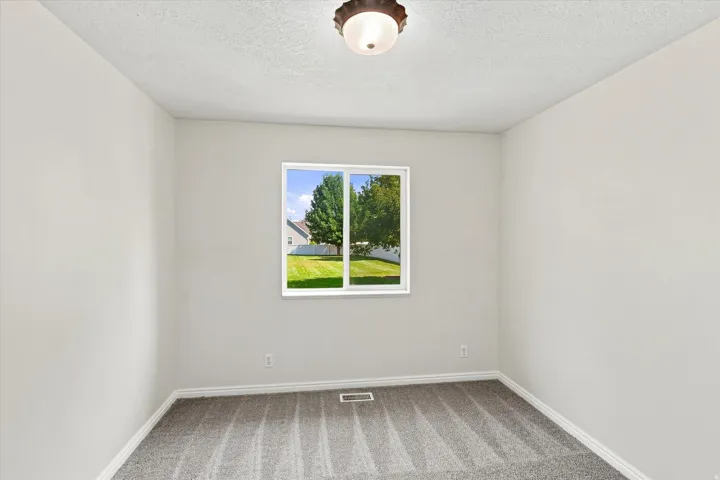 Bright room featuring a large window, neutral wall paint, and textured carpeting