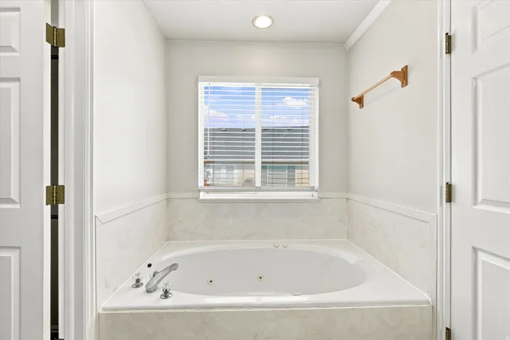 Built-in soaking tub with a tiled surround, recessed lighting, and a window with blinds