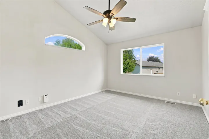 Vaulted ceiling with a ceiling fan, arched window, standard window, and light gray carpet flooring