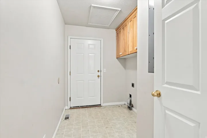 Utility room featuring light wood-finish cabinetry, patterned floor tiles, and a white paneled door
