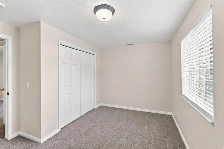 Light-colored walls, patterned carpeting, white window blinds, and white bi-fold closet doors