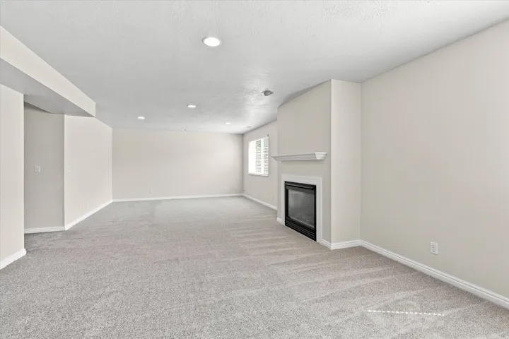 Recessed ceiling lighting, light gray carpeting, neutral wall finishes, fireplace with white mantel, and window with white shutters