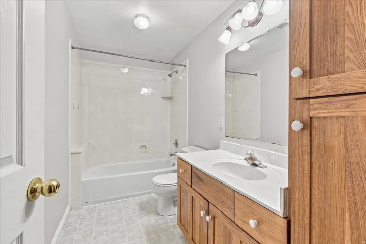 Bathroom featuring a wood-finish vanity with a single basin sink, integrated mirror, and a shower-tub combination