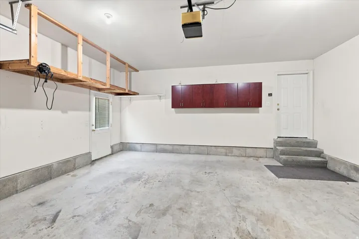 Attached garage featuring concrete flooring, built-in overhead storage, and wall-mounted cabinetry