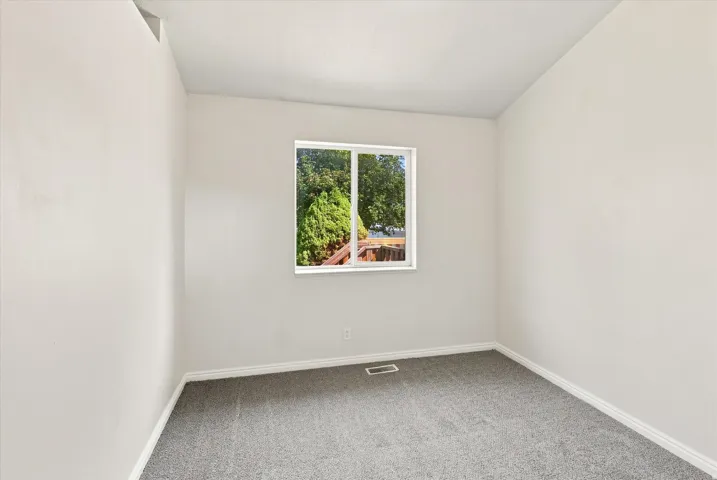 Grey carpet flooring, white painted walls, white trim, and a single window with white framing