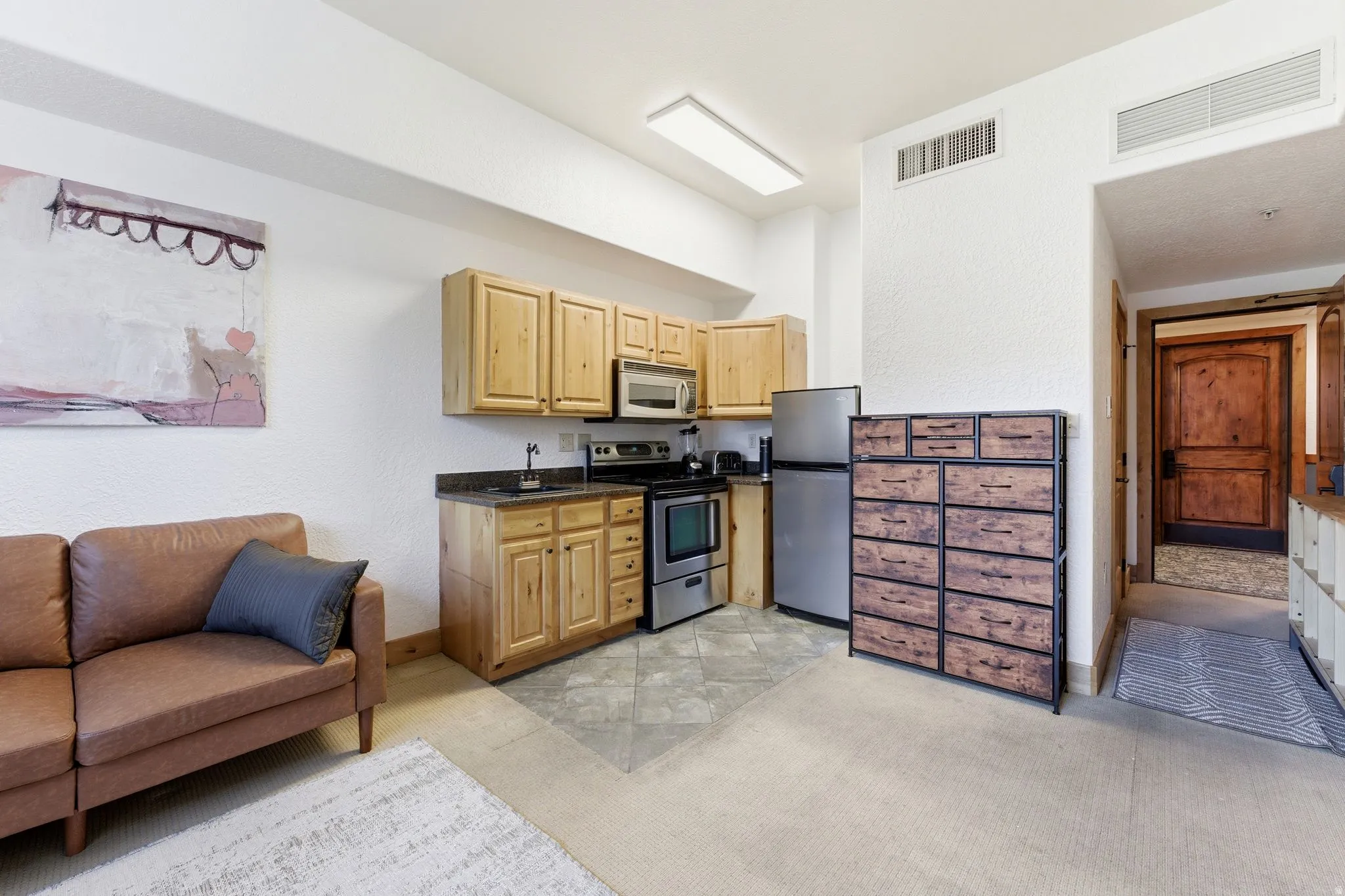 Compact kitchen area featuring wood-finish cabinetry, dark countertops, and stainless steel appliances