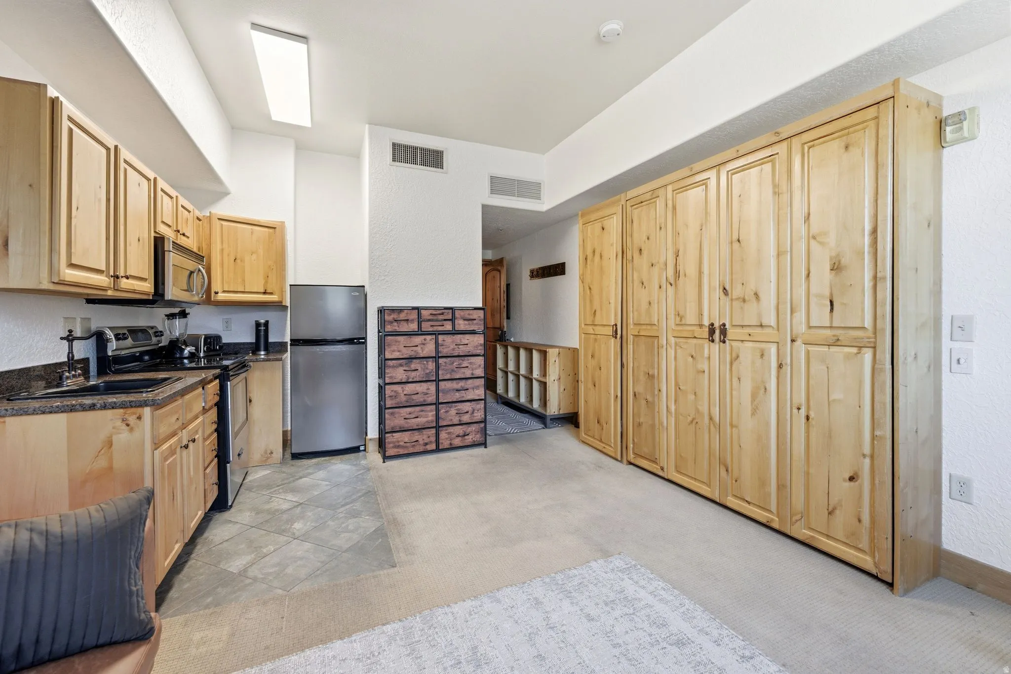 Kitchenette featuring wood cabinetry, dark countertops, and stainless steel appliances