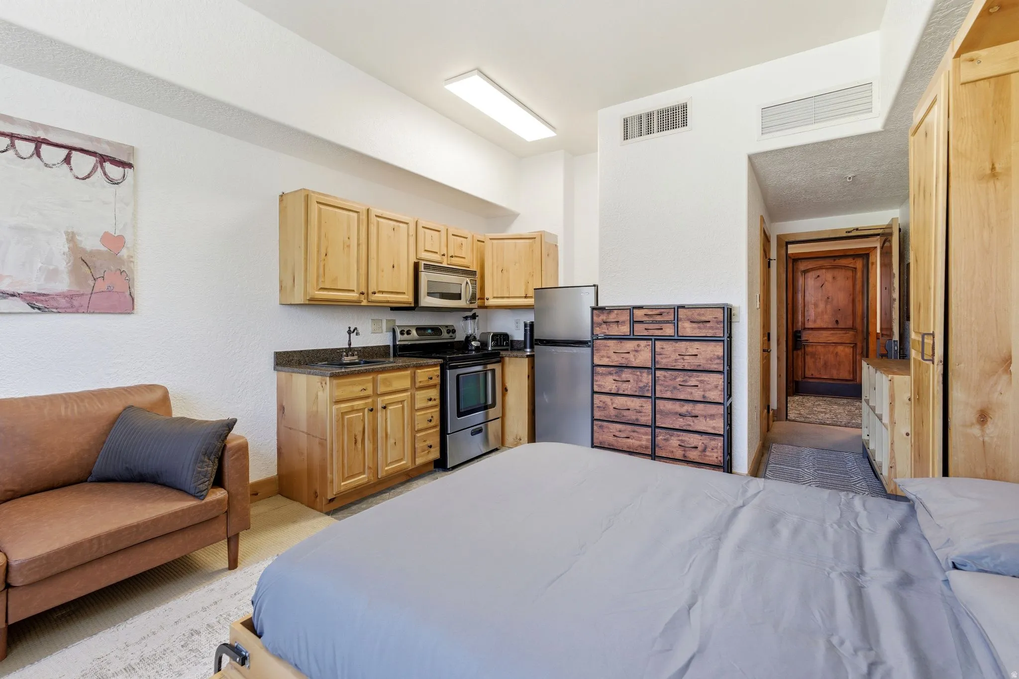 Compact living area featuring a full kitchen with light wood cabinetry, stainless steel appliances, and dark countertops