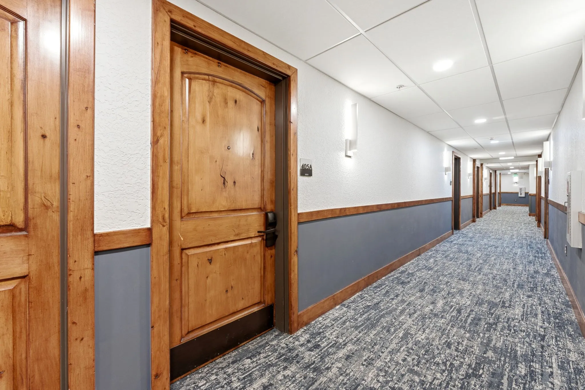 Hallway featuring textured white walls, a gray wainscoting, and wood trim detailing