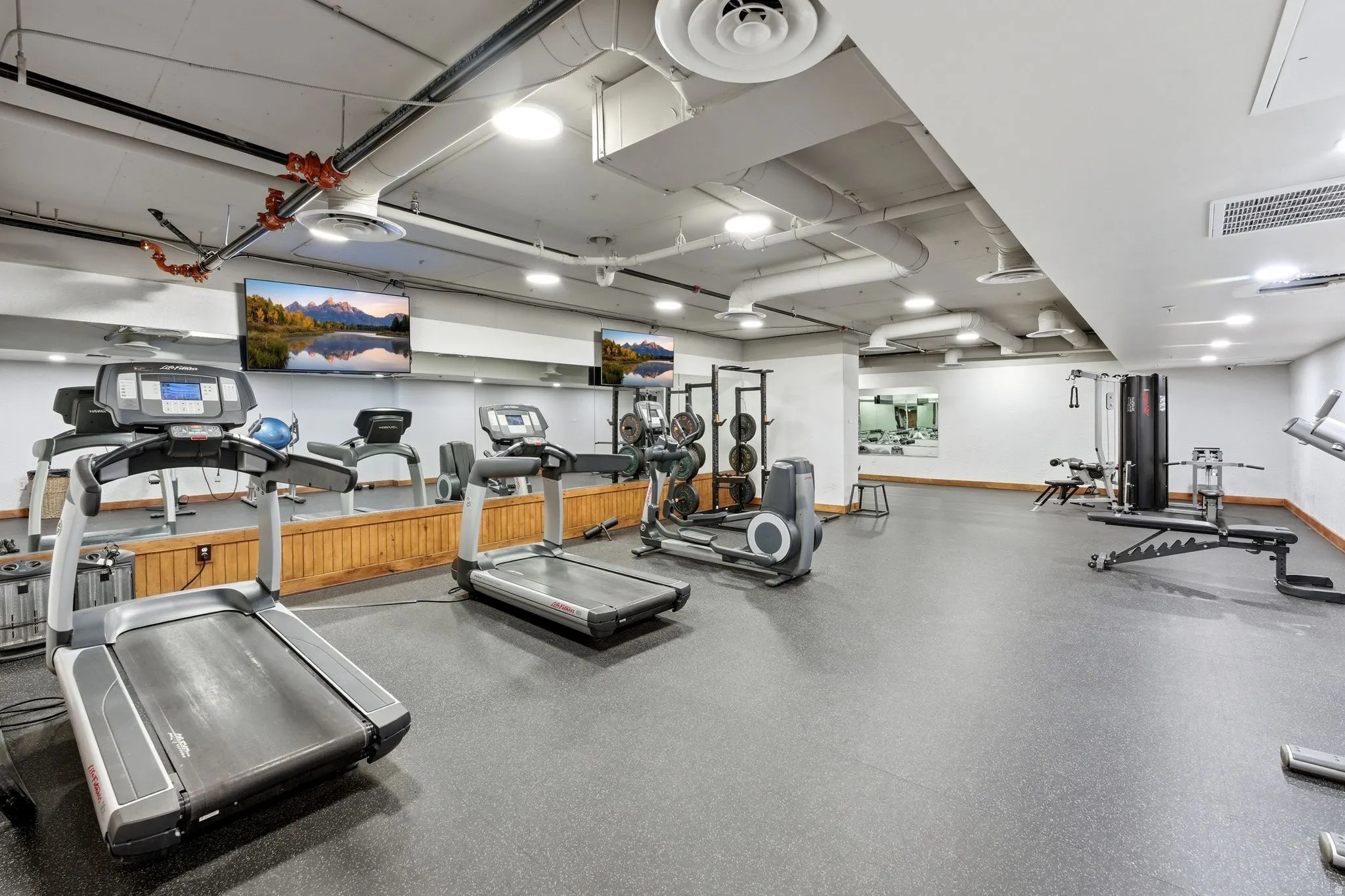 Fitness facility featuring durable rubber flooring, exposed ceiling ducts, and recessed lighting