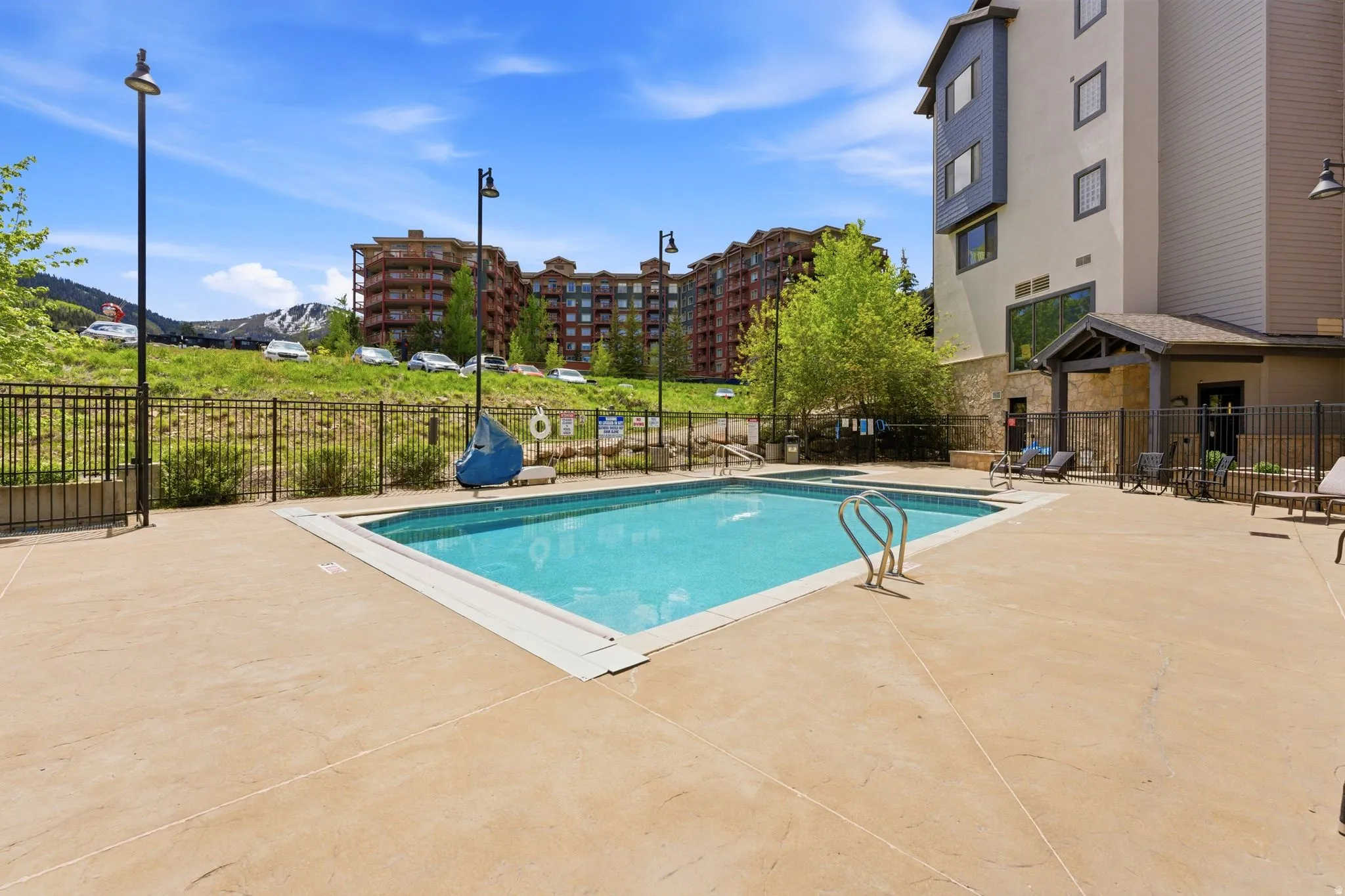 Outdoor swimming pool with concrete decking, surrounded by a black metal fence