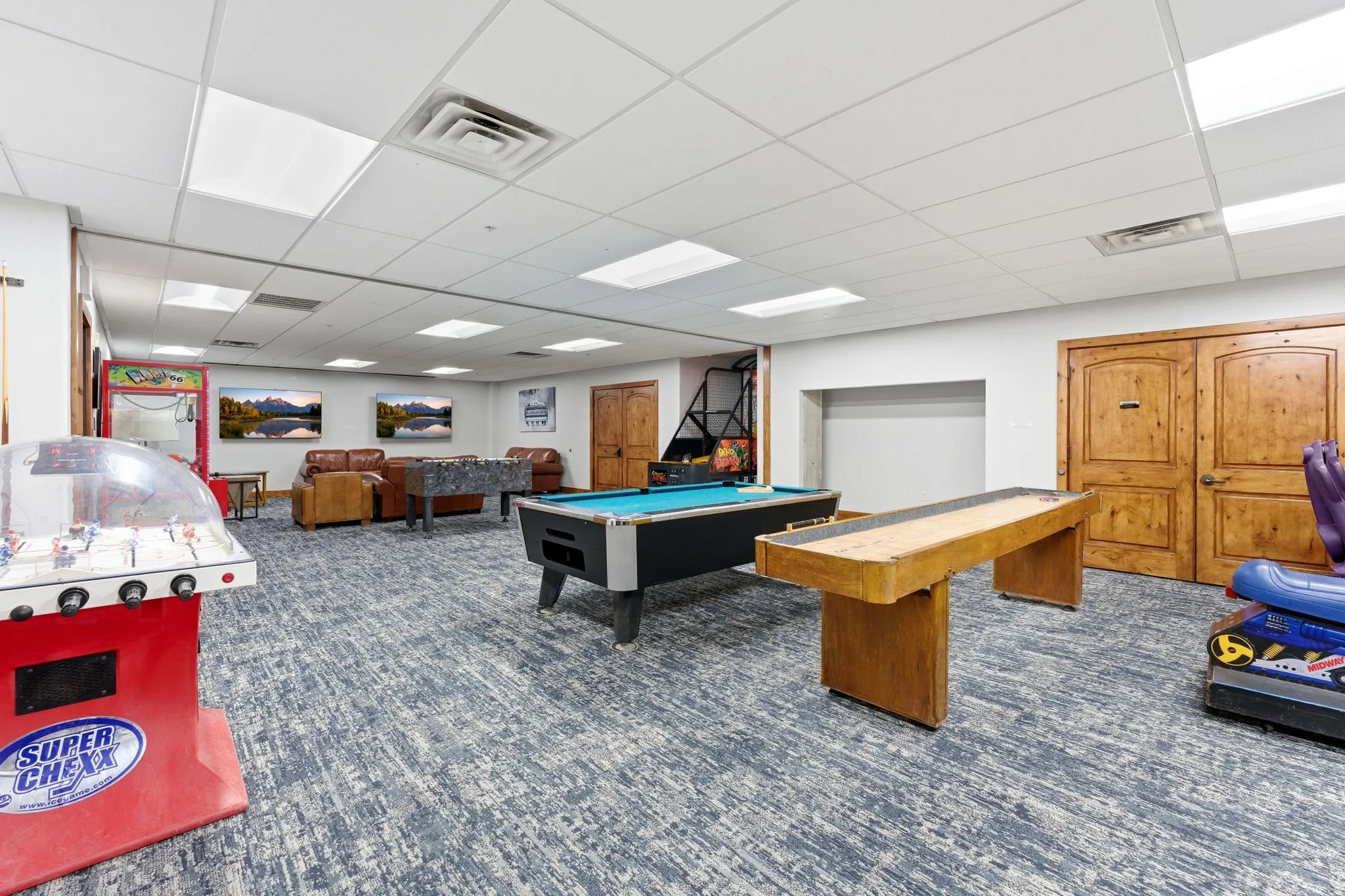 Spacious recreation room featuring patterned carpet flooring, white walls, and a dropped ceiling with integrated lighting