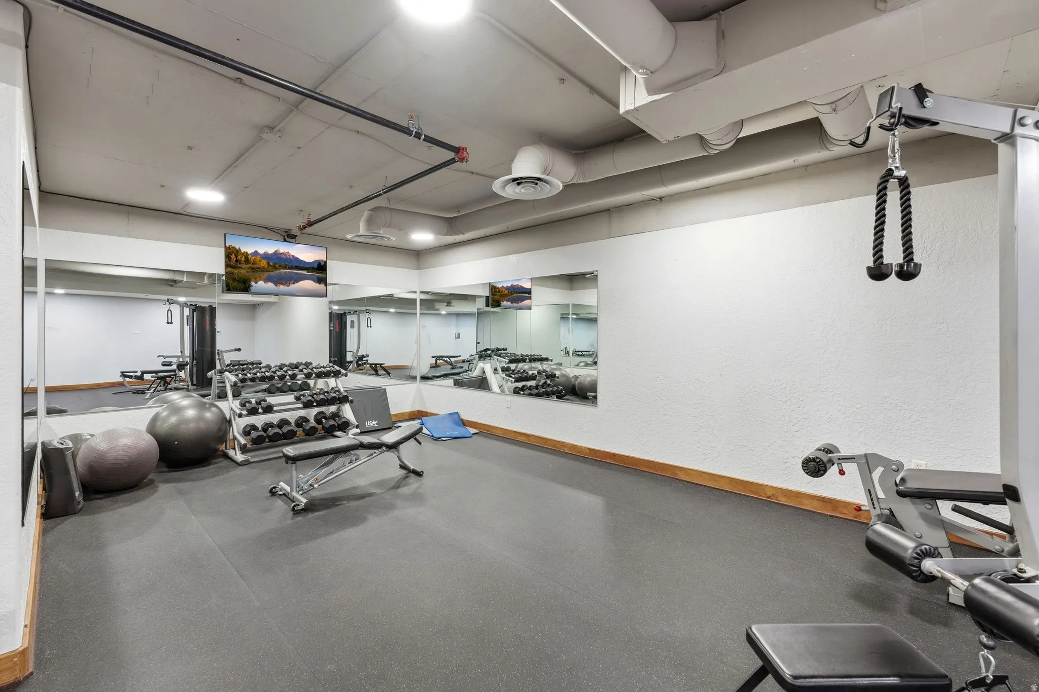 Dedicated fitness area featuring rubber flooring, mirrored walls, and exposed ceiling ductwork
