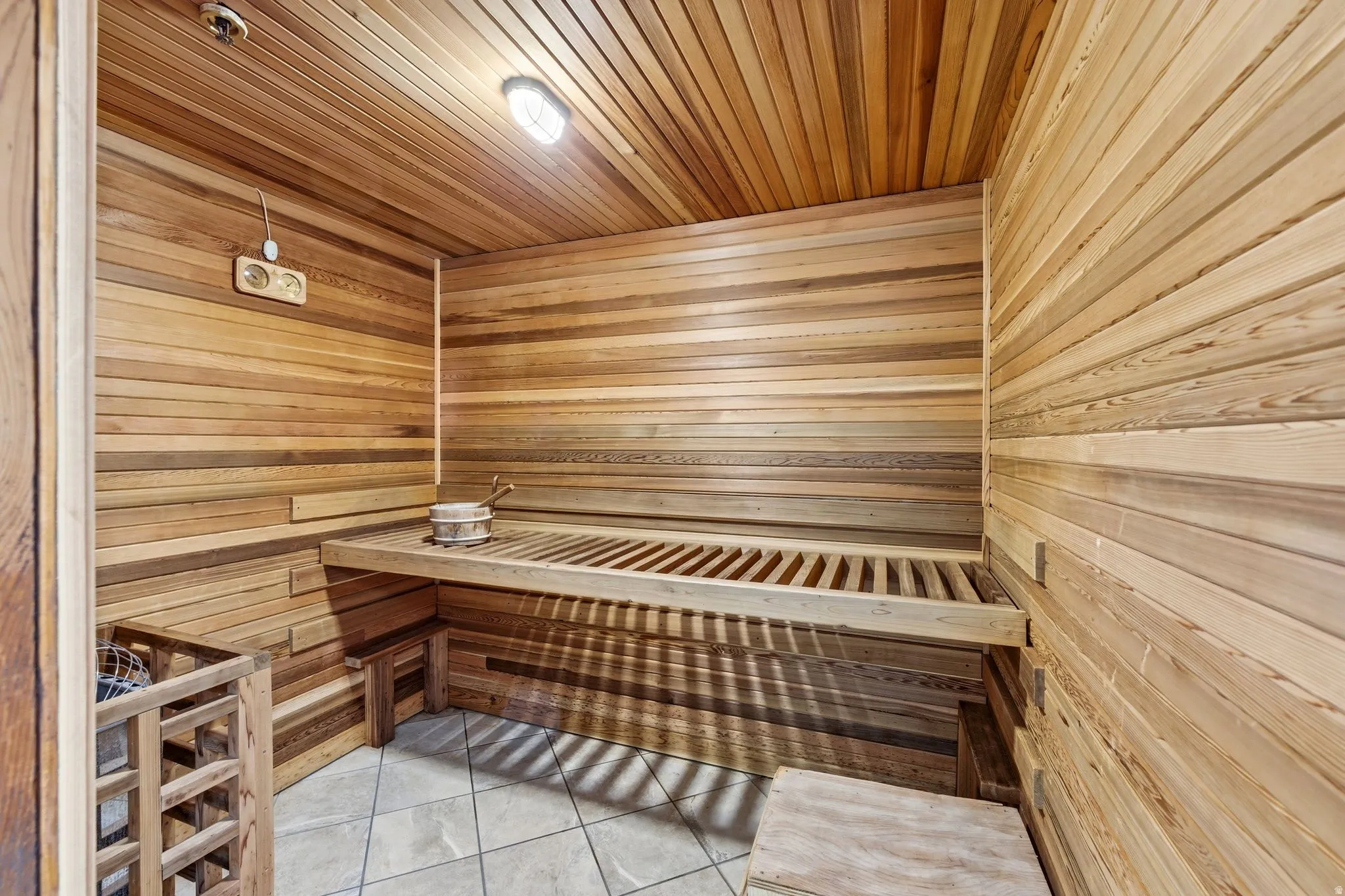 Built-in sauna featuring wood-paneled walls and ceiling, a slatted wood bench, and tiled flooring
