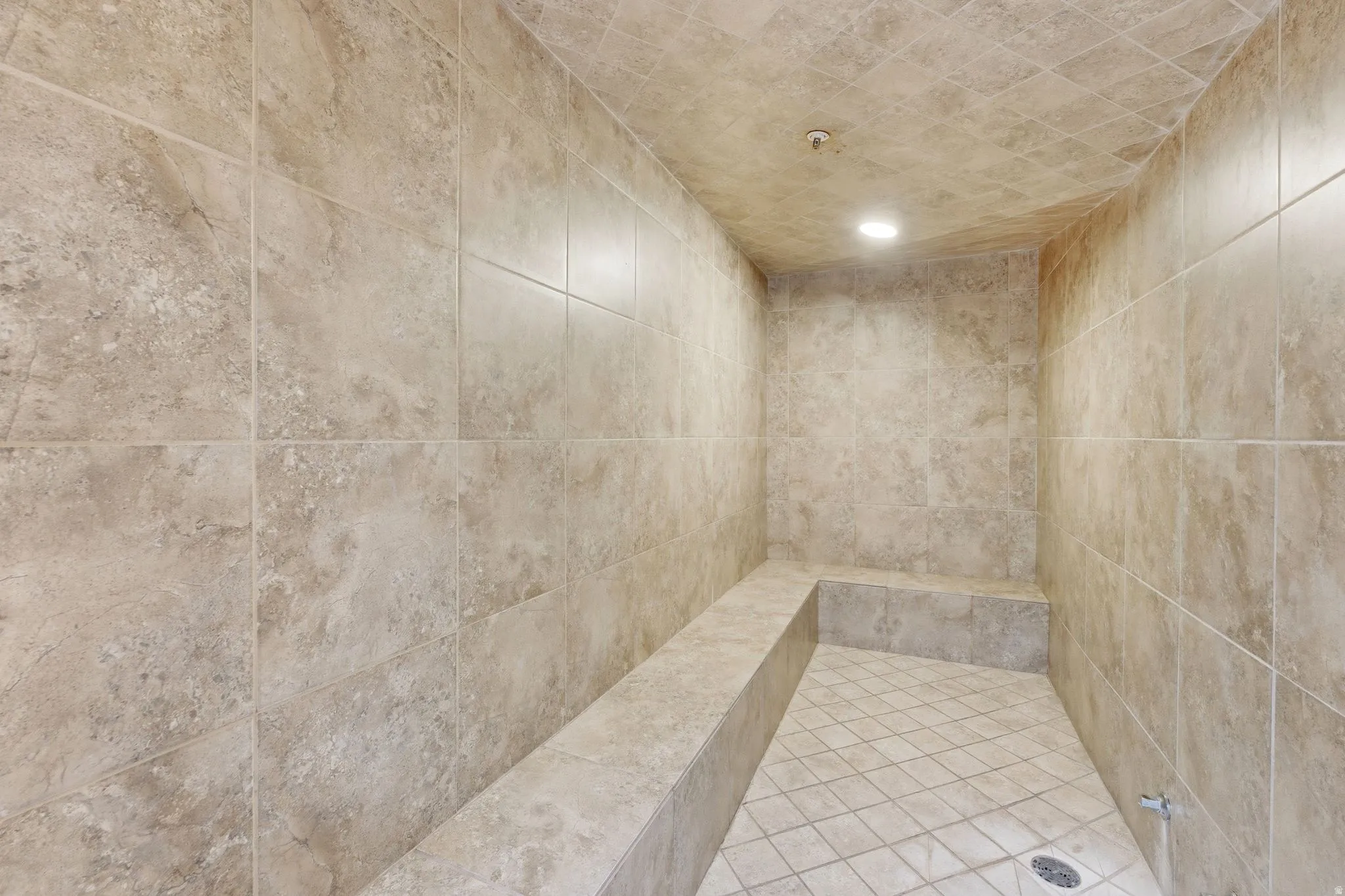 Spacious walk-in shower featuring full-height stone-look tile walls and ceiling