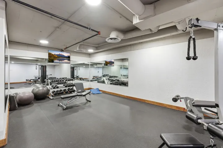 Dedicated fitness area featuring rubber flooring, mirrored walls, and exposed ceiling ductwork