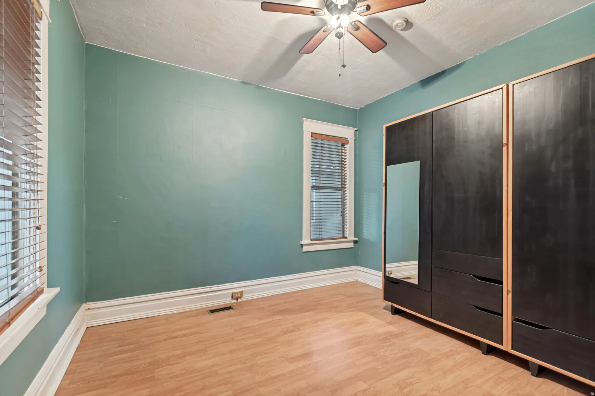 Room featuring wood-finish flooring, white baseboards, and two windows with blinds and white trim