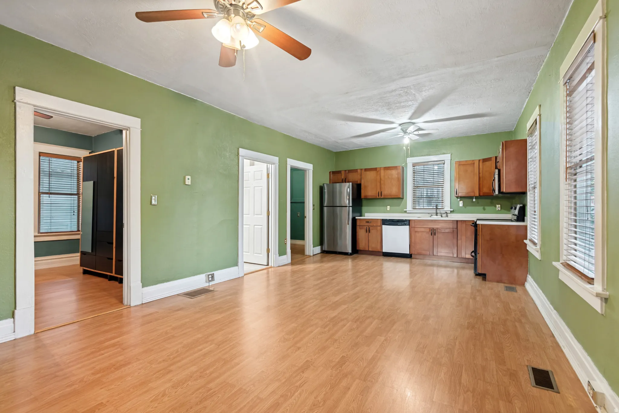 Open-concept living space featuring wood-finish flooring, a kitchen area with wood cabinetry, stainless steel appliances, and white countertops