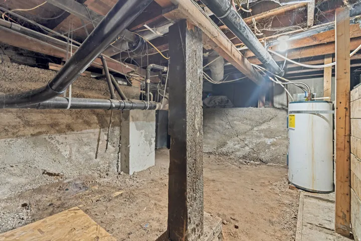 Utility area featuring a water heater, exposed concrete foundation walls, and overhead piping