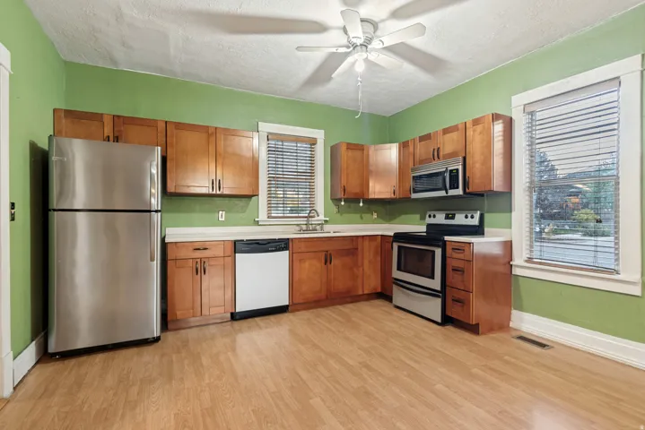 Kitchen featuring wood-finish flooring, wood cabinetry, stainless steel appliances, and a ceiling fan