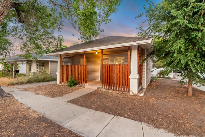 Front exterior featuring light gray horizontal siding, a covered porch with white columns, and a rich wood-tone slatted privacy fence
