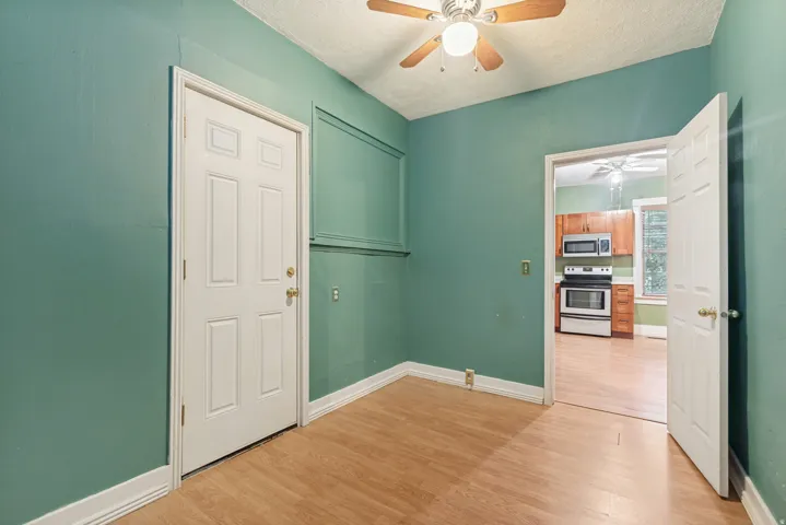 Interior room featuring wood-finish flooring, a ceiling fan with light fixture, and a doorway opening to a kitchen with wood cabinetry and stainless steel appliances