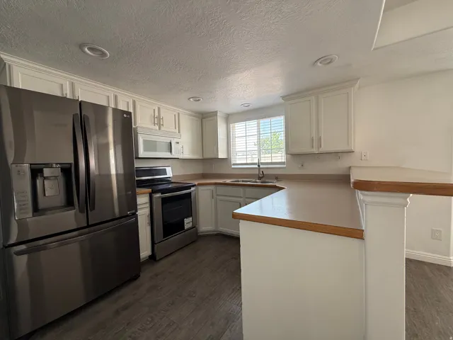 Kitchen featuring white cabinetry, light wood-finish countertops, stainless steel appliances, and wood-finish flooring