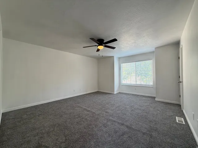 Spacious room featuring neutral carpeting, light-toned walls, and a ceiling fan with integrated lighting
