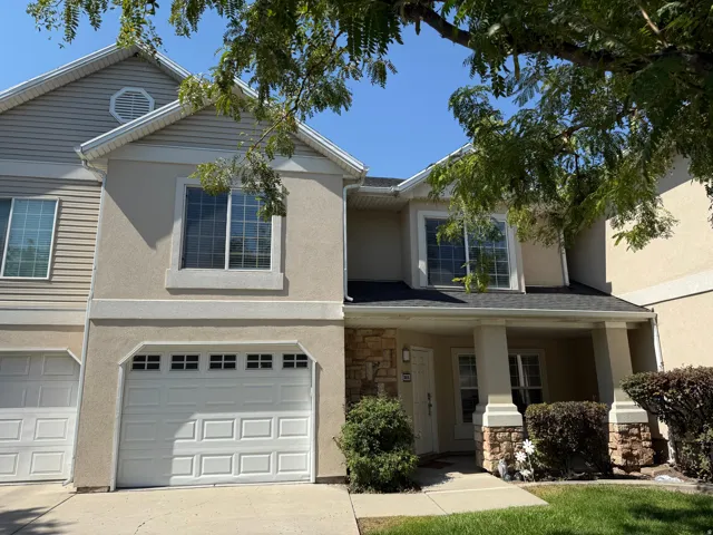 Two-story townhouse featuring a stucco and siding exterior, a covered front entry with stone-clad columns, an attached garage with a panel door, and mature landscaping