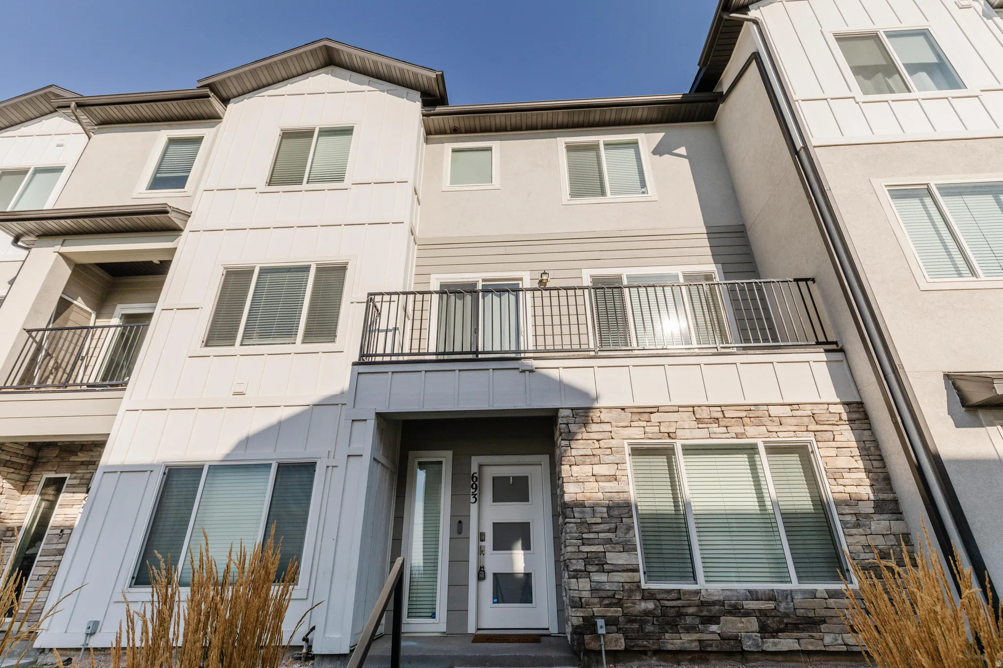 Contemporary multi-level townhome featuring a stone facade, white vertical siding, and a second-story balcony with dark railings