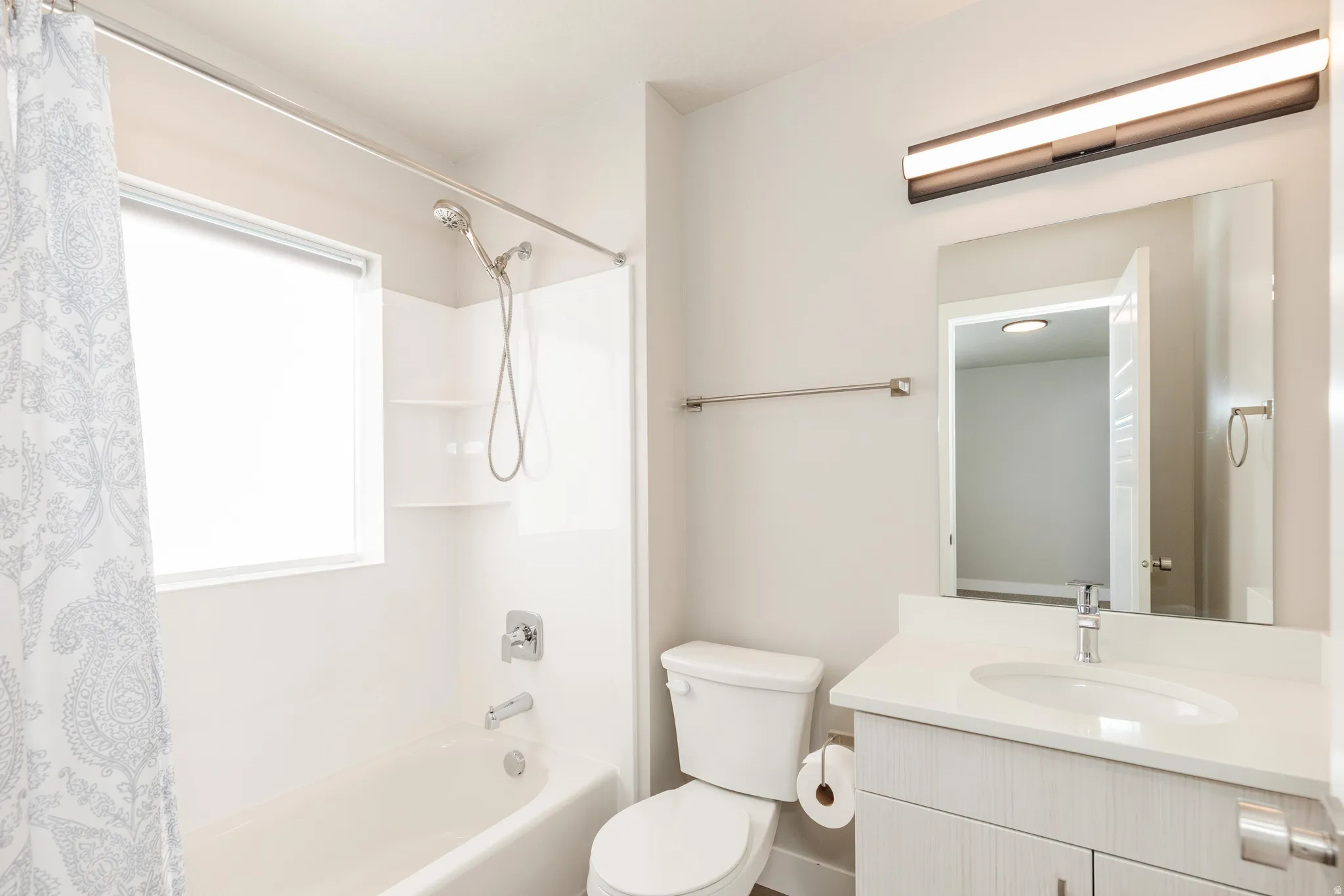 Bathroom featuring a full tub with shower, white vanity with integrated sink, contemporary vanity lighting, and a wall-mounted mirror