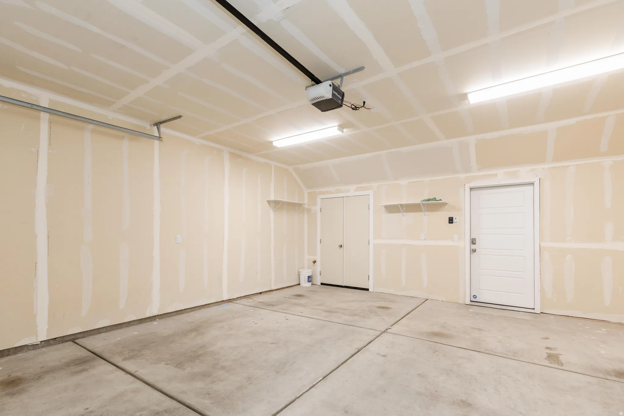 Spacious garage featuring a concrete floor, exposed drywall, overhead lighting, and an automatic garage door opener