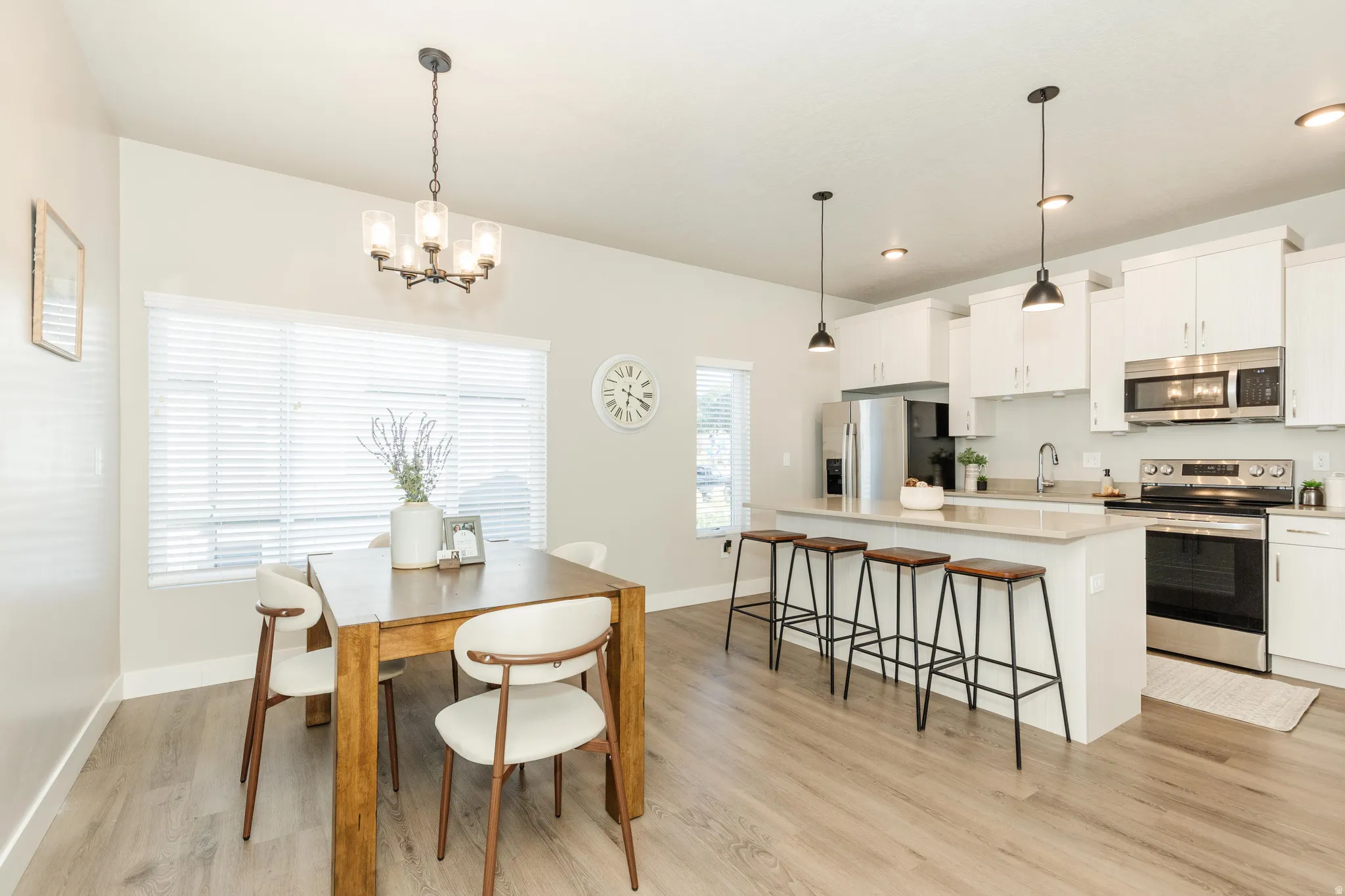 Open-concept kitchen and dining area featuring wood-finish flooring, white cabinetry, stainless steel appliances, and a kitchen island with pendant lighting